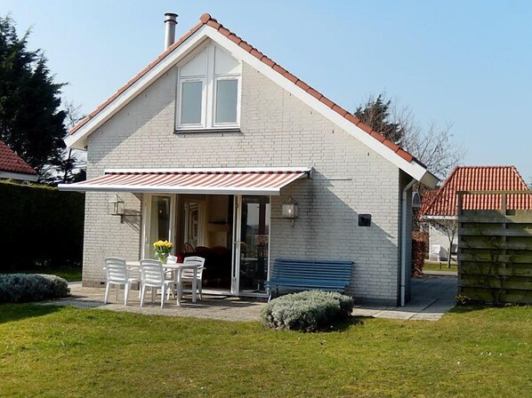 Et etplanshus med facade af mursten, rødt tegltag og en overdækket terrasse med hvide plastikstole og et bord.