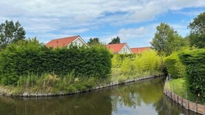 Una vista tranquila a orillas del río, con dos casas, abundante vegetación y una superficie acuática en calma.
