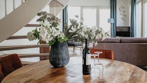 Un comedor con una mesa de madera, un florero con flores, una botella de vino y un televisor al fondo.