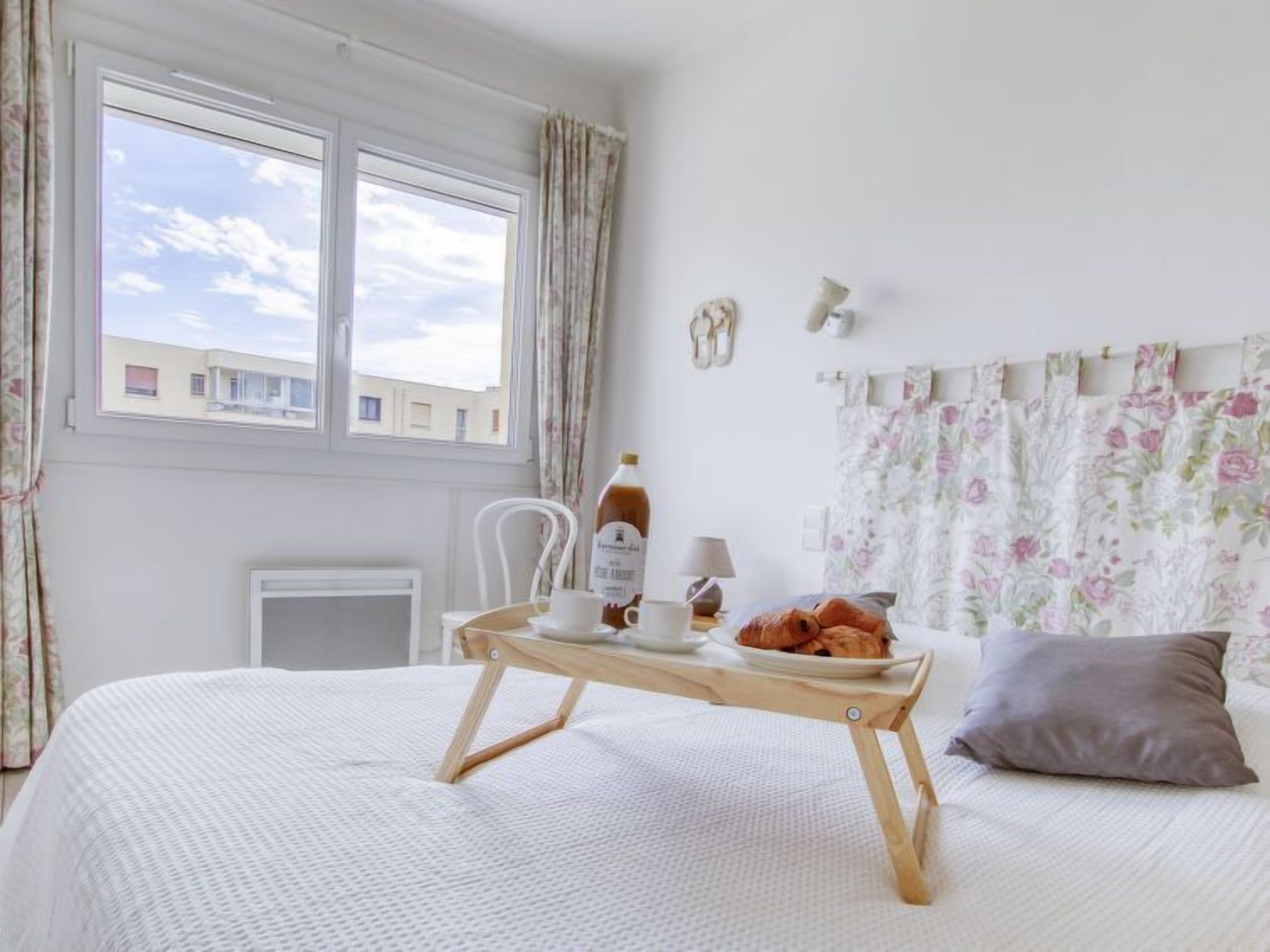 A bedroom with a bed, a bedside table with a tray, a bottle, and a cup.