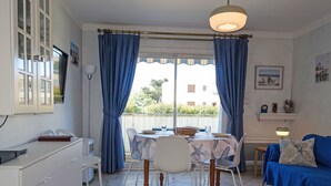 En matplats med ett bord dukat för två personer, en soffa och ett köksområde med ett vitt skåp och ett litet bord.