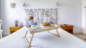 Ett sovrum med en säng, ett nattduksbord med en lampa, ett litet bord med frukosttillbehör och en blommönstrad gardin.