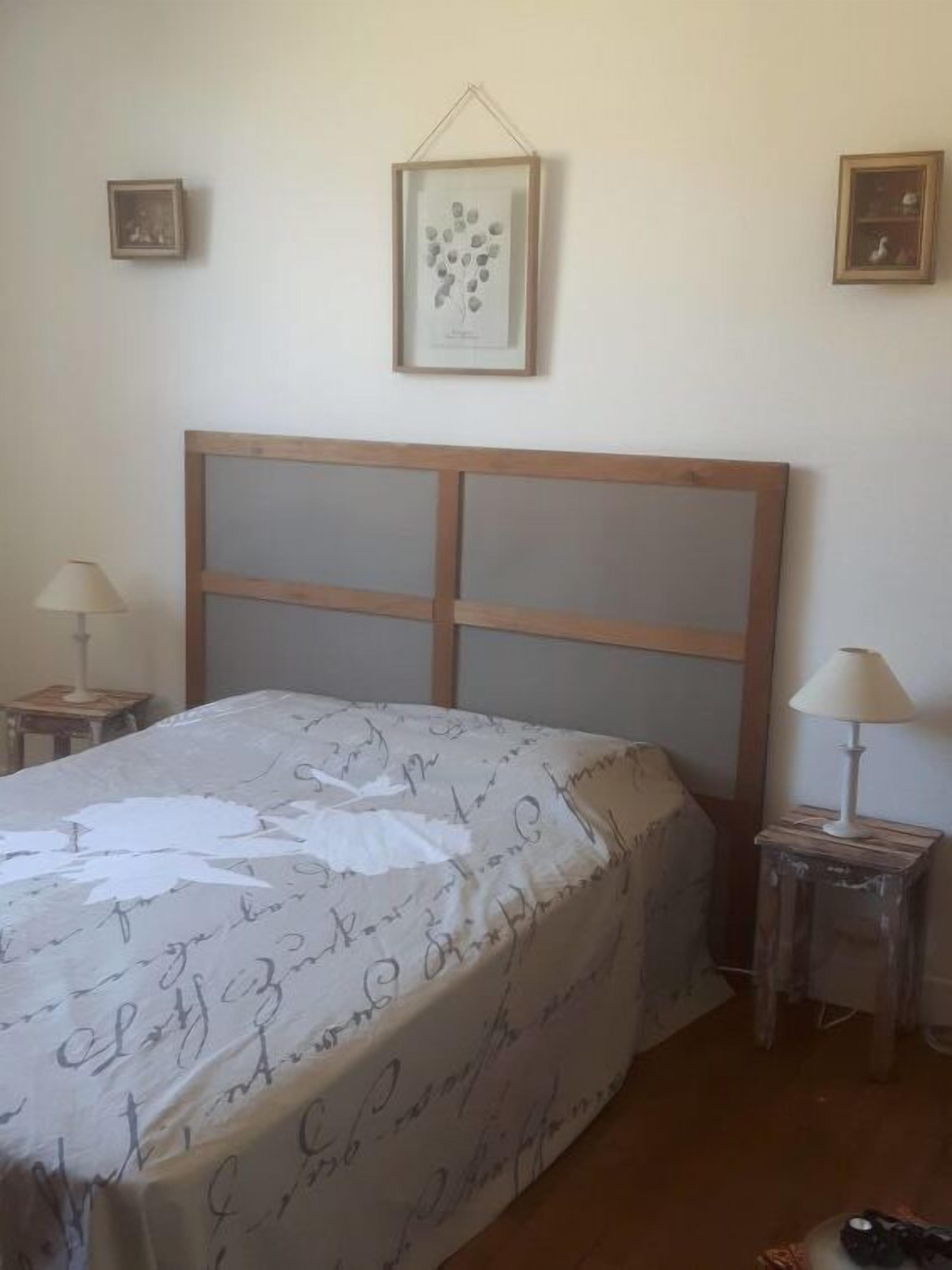 Ein Schlafzimmer mit einem hölzernen Kopfteil, einem Bett mit einem gemusterten Bettbezug, zwei Nachttischen mit Lampen und gerahmten Bildern an der Wand.