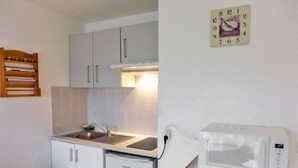 A compact kitchen with white cabinets, a sink, a small refrigerator, and a microwave on a wooden stand. - Hego Alde by Interhome (Bidart)