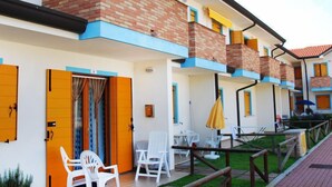 A multi-story hotel with a brick facade, blue trim, and yellow shutters. There are outdoor seating areas with white chairs and tables, and a small garden area. - Solmare by Interhome (Rosolina Mare)