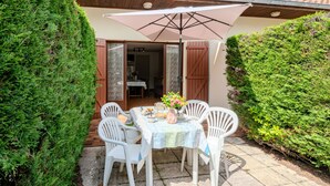 A patio with a table and chairs, a large umbrella, and a view of the house interior. - Vacation home Sicard by Interhome (Mimizan)