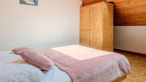 A bedroom with a wooden ceiling, a bed with pink bedding, and a wardrobe. - Vacation home Sicard by Interhome (Mimizan)