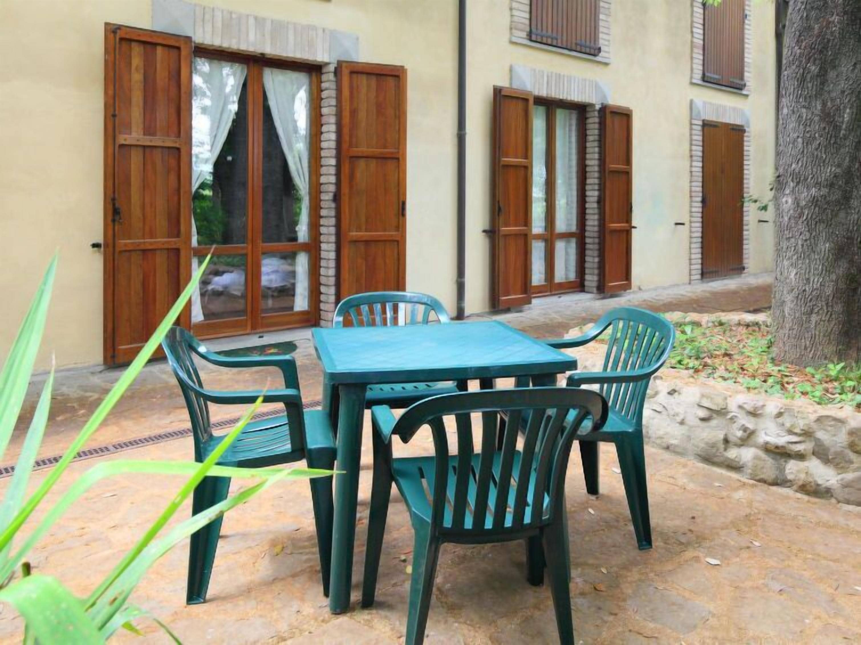 An outdoor seating area with a table and chairs, a stone-paved patio, and wooden doors with shutters.