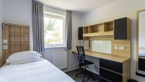 A hotel room with a bed, a desk, a chair, a radiator, and a window with curtains. - University Campus Park Wood by Interhome (Canterbury)