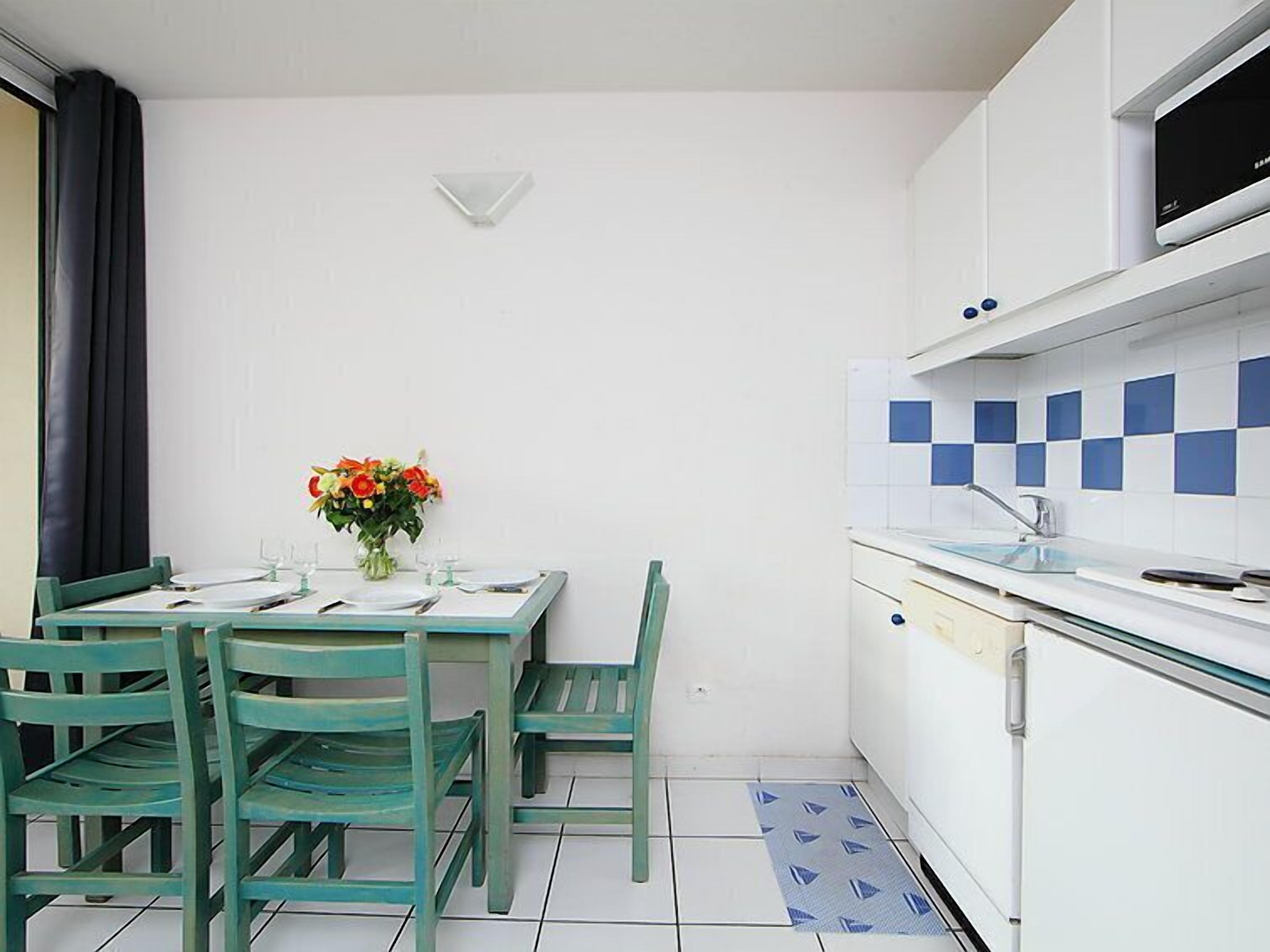 Een compacte keuken met witte kastjes, een betegelde spatwand, en een klein eethoekje met een tafel en stoelen.