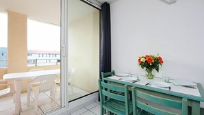 Een balkon met een eettafel gedekt voor twee personen, een vaas met bloemen en uitzicht op de stad.