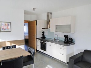Cocina moderna con armarios blancos, encimera negra y extractor de acero inoxidable. Cuenta con una zona de comedor con una mesa de madera y sillas negras.