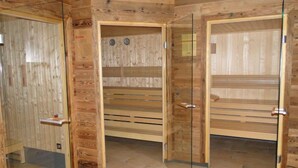 Ein Saunaraum mit Holzwänden und -bänken, Glastüren und einem gefliesten Boden.