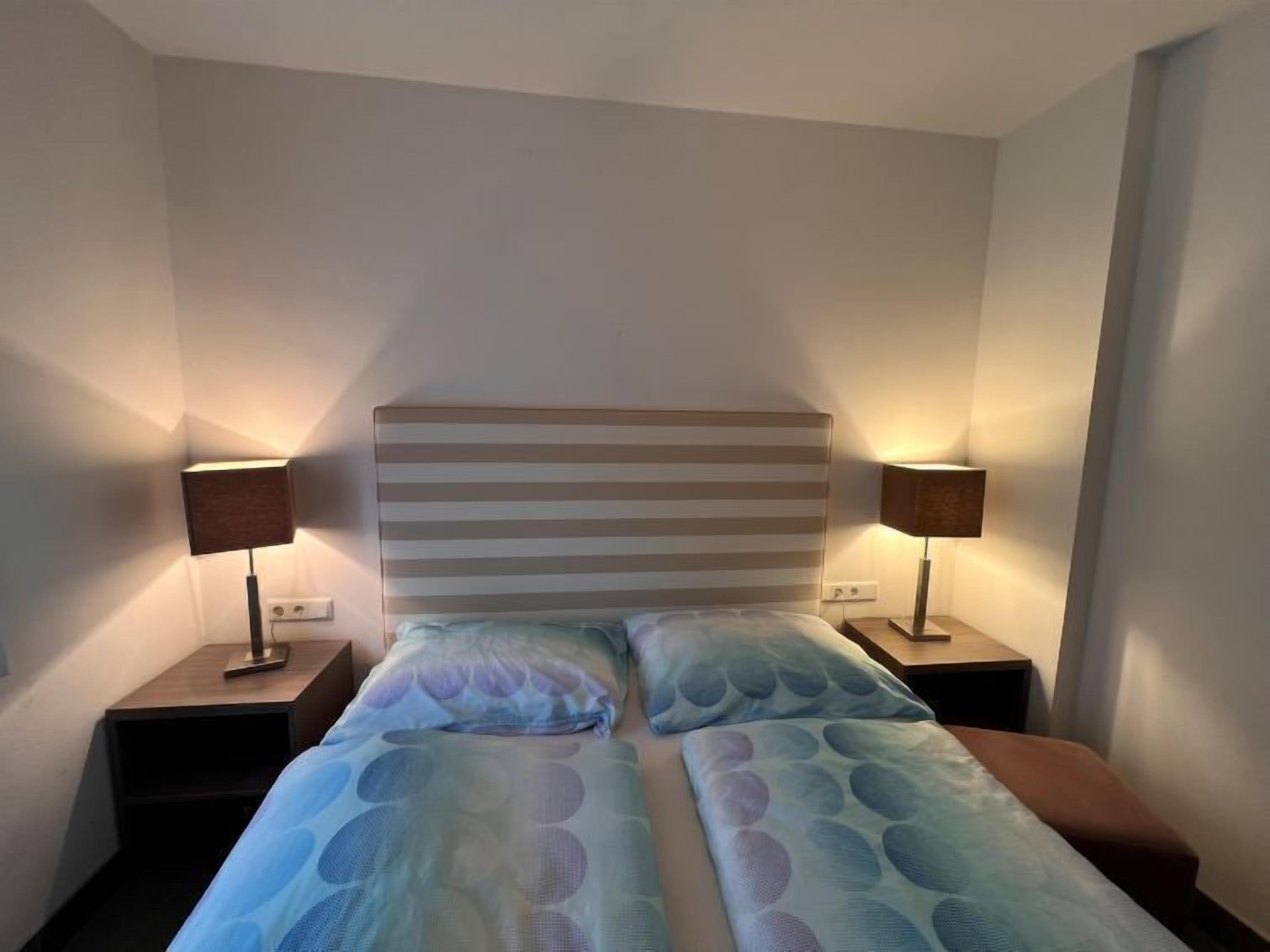 A hotel room with a bed, two bedside tables, and two lamps.