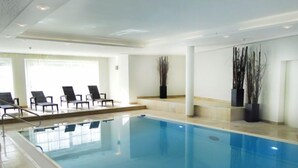 Ein großes Hallenbad mit klarem, blauem Wasser, umgeben von Liegestühlen und Topfpflanzen.