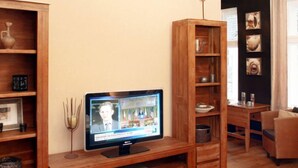 Una sala de estar con una unidad de entretenimiento de madera, un televisor mostrando un noticiero y una zona de comedor con una mesa y sillas.