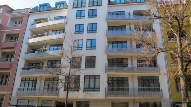 Un edificio residencial de varios pisos con balcones, una entrada visible y automóviles estacionados.