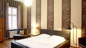 Habitación de hotel con cama, mesita de noche, silla, lámpara de pie y ventana con cortinas.