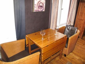 A wooden table with two chairs, a picture of a rose on the wall, and a window with curtains.