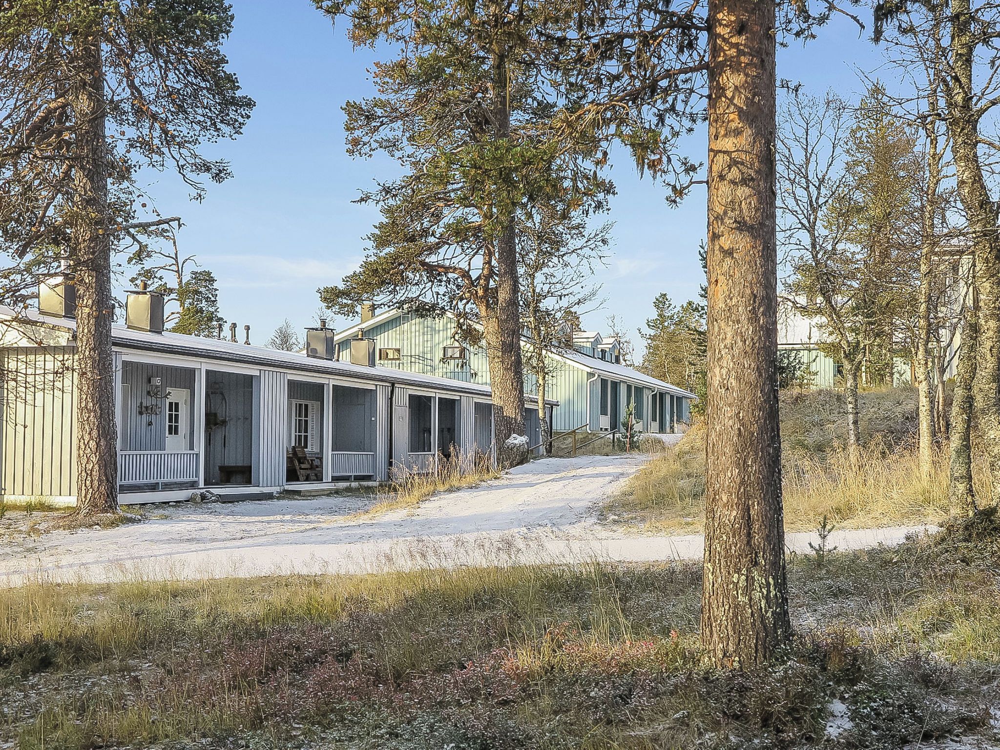 Une rangée de cabanes dotées d’un porche abrité, entourées d’arbres et baignées par un ciel dégagé.