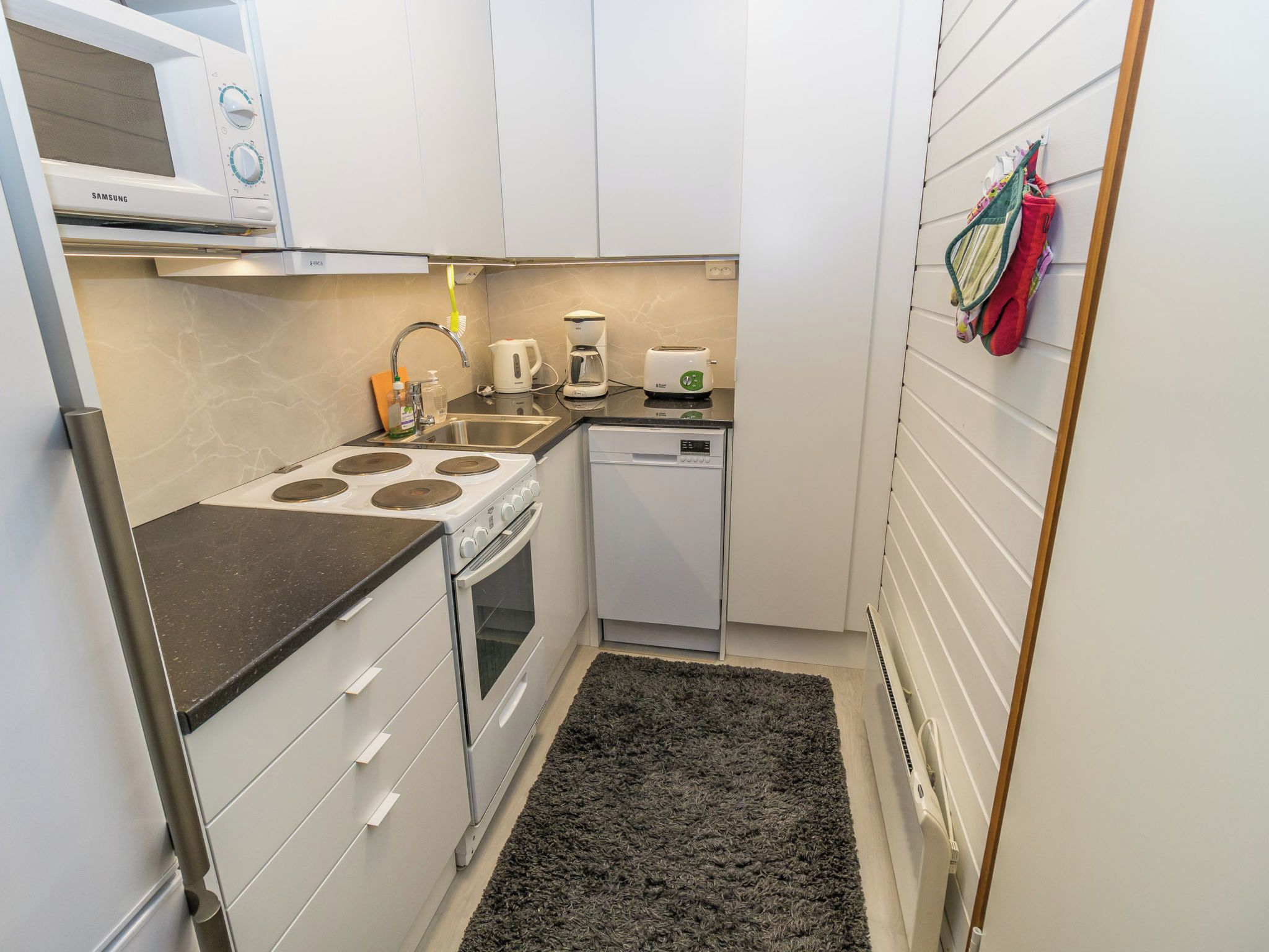 Een kleine keuken met een magnetron, kookplaat, spoelbak en vaatwasser.