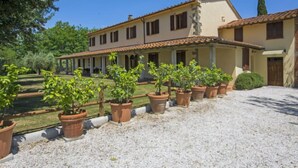 Un grand bâtiment à deux étages, doté d’un toit en tuiles et de nombreuses fenêtres. On y trouve un patio couvert agrémenté de plantes en pot et une allée gravillonnée.