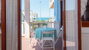 An outdoor balcony with a table and chairs, a view of the sea, and buildings in the background.