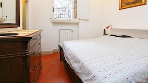 A bedroom with a bed, dresser, radiator, window, and a painting on the wall. - Pantheon by Interhome (Rome: Historical City Center)