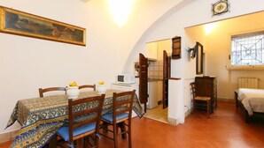 A dining area with a table set for four, a kitchen in the background, and a bedroom with a bed and a window. - Pantheon by Interhome (Rome: Historical City Center)