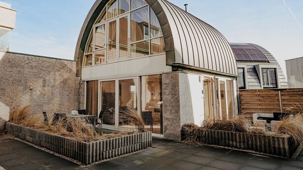 Une maison moderne dotée d’un toit incurvé et de grandes fen êtres.