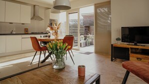 Une cuisine moderne avec des meubles blancs, une table à manger entourée de chaises orange et un téléviseur posé sur un meuble en bois.