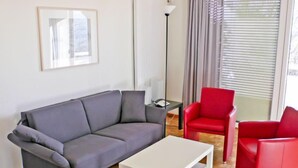 Un saló modern amb un sofà gris, una taula de centre blanca i butaques vermelles.