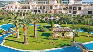 Un resort con una grande piscina, palme e un edificio in stile mediterraneo sullo sfondo.