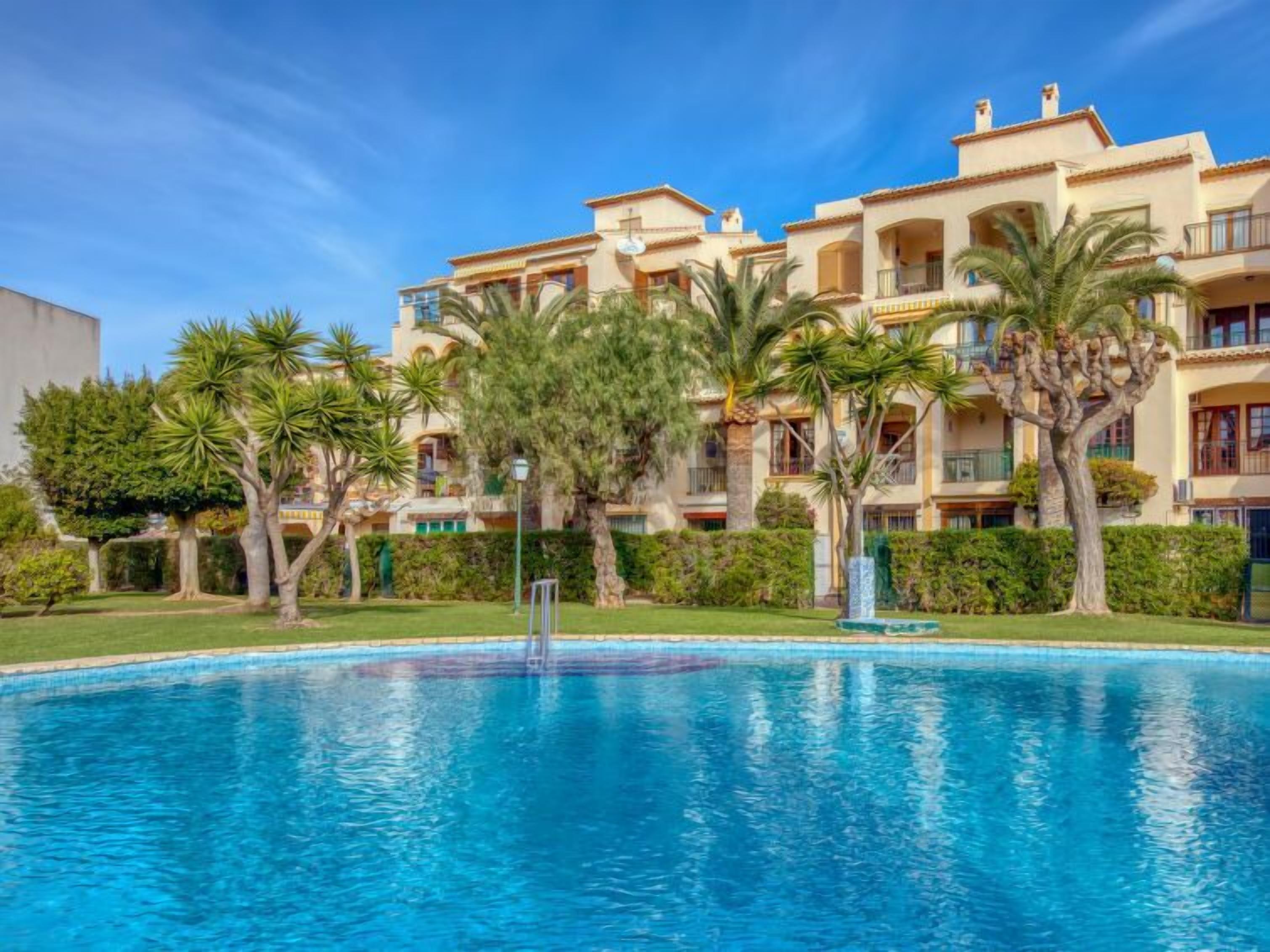 A hotel with a swimming pool surrounded by palm trees and a well-maintained lawn.