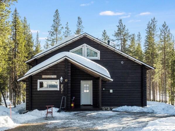 A wooden cabin with a gabled roof, a front door, and a window.