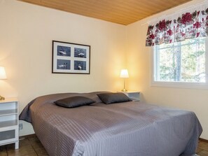 A bedroom with a bed, two bedside tables, a window with curtains, and a wall-mounted picture. - Levijoutsen by Interhome (Kittilä)