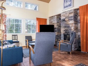 A cozy living room with a stone fireplace, comfortable seating, and large windows.