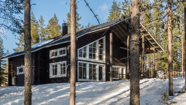 A cabin with a large windowed front section, surrounded by trees and snow.