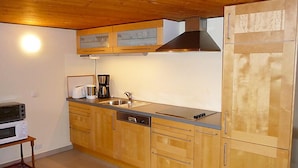 A compact kitchen with wooden cabinets, a built-in oven, a coffee maker, and a stainless steel sink.