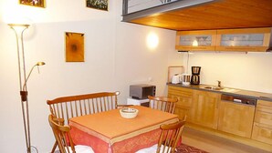 A compact kitchen with wooden cabinets, a dining table with chairs, a floor lamp, and a rug.