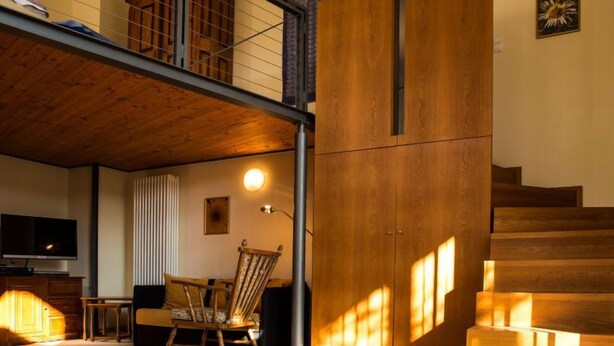 A modern living room with a wooden staircase, a TV, and a patterned rug.