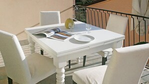 A white table with two chairs, a magazine, a glass, and a plate on a balcony with a railing. - Apartment Milano by Interhome (Forte dei Marmi)