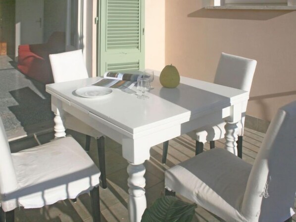 Una mesa blanca con un vaso y un libro encima, una puerta verde y una silla roja al fondo.