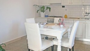 A white dining table with chairs, a potted plant, and kitchen appliances in the background. - Apartment Milano by Interhome (Forte dei Marmi)