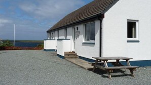 A white building with a tiled roof, a small window, and a picnic table. - Alan's House by Interhome (North Skye)