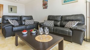 A modern living room with two black leather sofas, a wooden coffee table, and a painting on the wall.