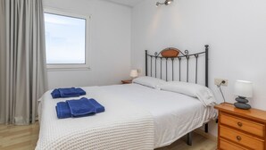 A neatly made bed with white linens and blue towels, a wooden nightstand with a lamp, and a window with curtains.