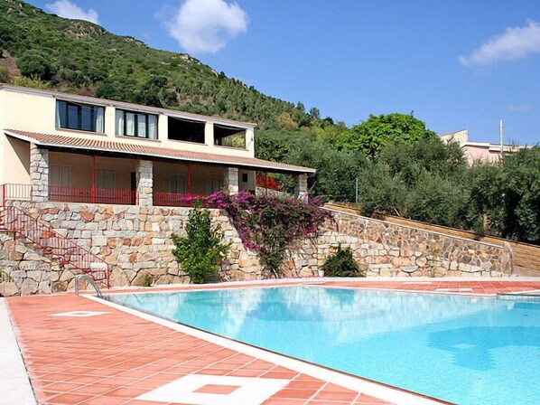 A modern building with a stone facade, a swimming pool, and a hillside backdrop.
