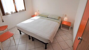 A bedroom with a bed, two bedside tables, a chair, and a window with curtains. - Casa Daniela by Interhome (Rosolina Mare)
