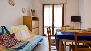 A cozy room with a bed, a dining table with chairs, a television on a stand, and a window with curtains. - Casa Daniela by Interhome (Rosolina Mare)